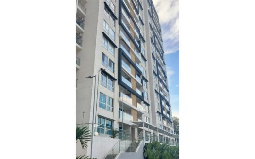 Tall modern apartment building with glass balconies and a grey facade, stairs and greenery at ground level.