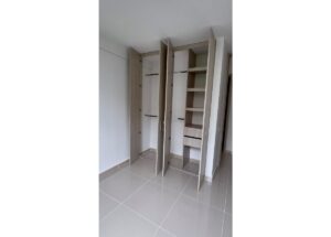 Three-door built-in wardrobe in a bright room: left and center sections with hanging rods, right section with shelves and drawers in a light wood finish.