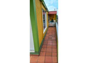 Outdoor balcony hallway with orange walls, green trim, and terracotta floor tiles leading to a storage area under a red awning at the far end