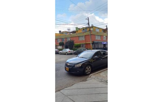 Black sedan parked on a curb beside a colorful two-story building under a blue sky with power lines overhead