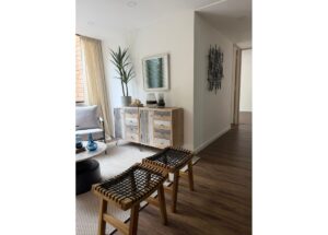 Living room with a rustic wooden sideboard, tall plant, wall art, and woven wood stools on a hardwood floor.