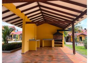 Covered outdoor barbecue area with brick grill, two granite counters, yellow walls, and terracotta tile floor in a sunny yard.