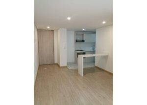 Open-plan living area with light wood floors and a white kitchen, including a breakfast bar.