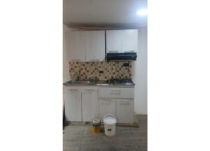 Compact kitchen with white cabinets, sink, and gas stove; paint bucket and can on the floor indicate renovation inertia.