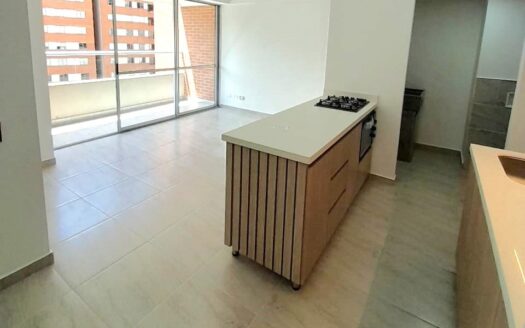 Open-plan kitchen with an island stove, light wood drawers, and a large glass balcony door letting in natural light.