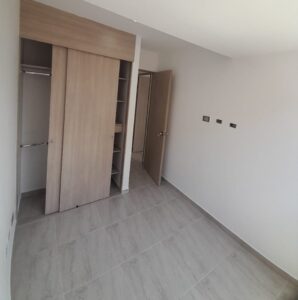 Room with light wood built-in wardrobe, open sliding doors showing shelves and hanging rod, empty space with gray tiled floor and white walls.
