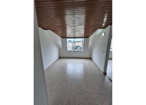 Empty, unfurnished room with white walls, a sloped wooden ceiling, and a large window showing a city view.