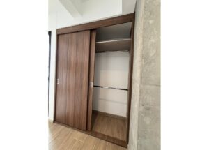 Wooden sliding closet doors open to reveal two shelves and a hanging rod inside.