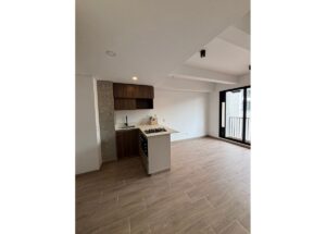Open-concept kitchen with an island stove, dark wood cabinets, and a light countertop; large windowed door to a balcony on the right.