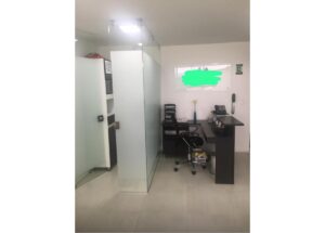 Small office with a glass partition, a desk and black chair, phone on desk, and a whiteboard with green scribble on the wall.