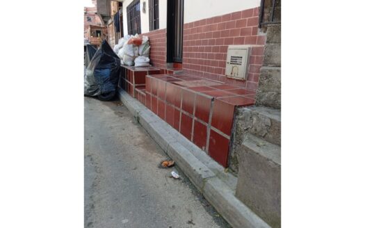 Red tiled steps along a building with a pile of garbage bags on the left and a metal mailbox on the wall