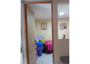 Door opens to a small child’s room filled with toys, a blue laundry basket, and a pink tablecloth on a bed or table, with framed pictures on yellow walls.