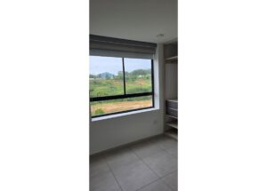 Empty room with tiled floor and a large window showing green countryside and hills; built-in shelves on the right.
