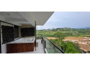 Balcony with a rectangular wooden hot tub on the left and a glass railing overlooking a green valley.