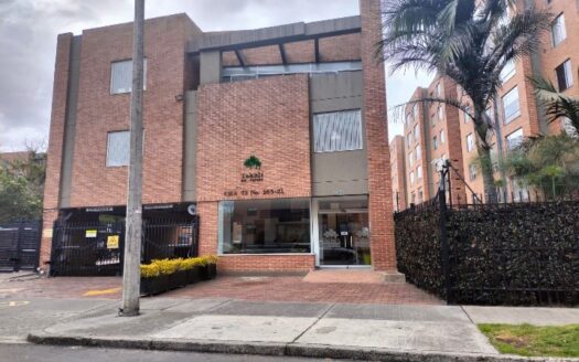 Brick apartment building with a glass lobby entrance and metal gates on either side; a palm tree stands to the right.