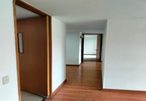 Interior hallway with light wooden floor, white walls, and open doorways leading to additional rooms.
