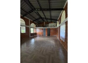 Empty brick-walled room with a mezzanine loft, arched windows, and metal roof trusses; tiled floor throughout.