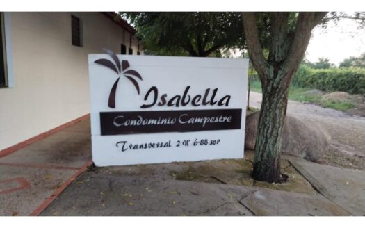 Sign reading 'Isabella Condominio Campestre' with a palm tree logo on a white panel beside a tree and driveway edge.