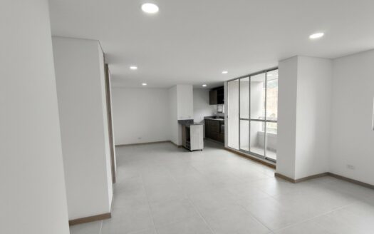 Empty open-plan living area with a small kitchen at the back, gray tile floor, white walls, and large glass doors to a balcony.