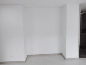 Empty white corner alcove with light gray floor tiles; doorway to a dark-tiled bathroom on the right.
