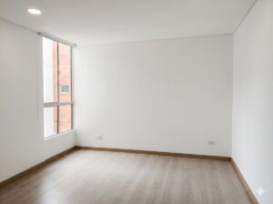 Empty white room with light wood flooring, large left window, and wooden baseboards; bright and minimal interior.
