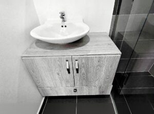 White oval sink on a wood-grain vanity with a chrome faucet in a modern bathroom.