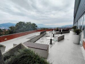 Rooftop terrace with minimalist concrete benches and planters, overlooking a distant city under a cloudy sky.