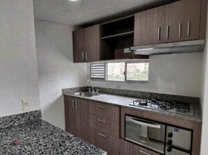 Compact kitchen with granite counters, dark wood cabinets, stainless steel sink, and four-burner gas stove under a range hood; window with a city view behind.
