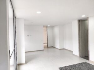 Empty, modern living space with white walls, light gray floor tiles, and recessed ceiling lights; glass door on the left and a gray wooden door on the right.