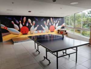 Indoor recreation room with a table tennis table in the foreground and a bowling-themed mural on the back wall showing pins and bowling balls.