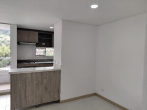 Empty modern kitchen with a wooden island and white countertop, visible stove area and upper cabinets.