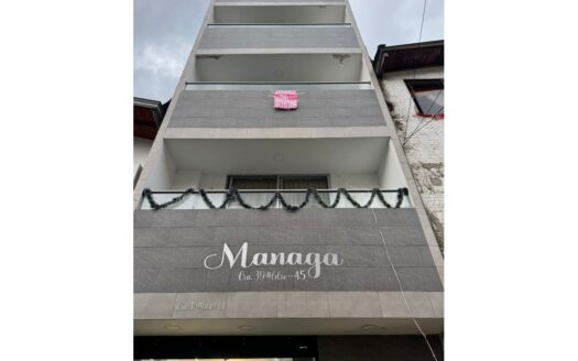Tall gray multi-story apartment building with balconies; a pink rent sign on the second-floor balcony and festive garland draped along the railing.