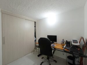 Home office setup: desk with computer monitor and office chair in a small room, sliding-wood wardrobe on the left.