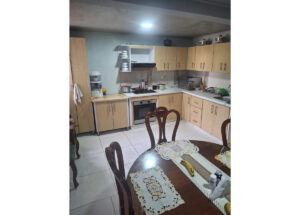 Cozy kitchen with lightwood cabinets, stove and oven, and a round dining table with lace doilies and bananas on it