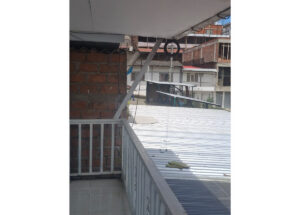 Balcony with white railing and brick wall, metal roof panels in foreground, and a street with brick buildings under construction in the background; a circular tire swing hangs from a pole.