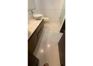 Small modern bathroom with beige countertop, white vessel sink, and brown vanity cabinets; toilet and glass shower at the back.