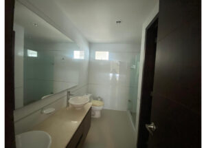 Modern bathroom with a beige countertop, vessel sink, and chrome faucet, mirrored wall, toilet, and glass shower enclosure.