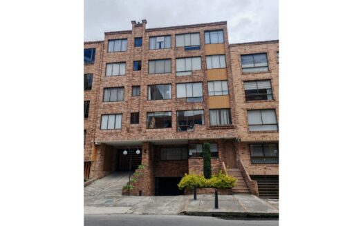 Brick apartment building with multiple windows, a gated entrance, and a small landscaped front area on a city street.