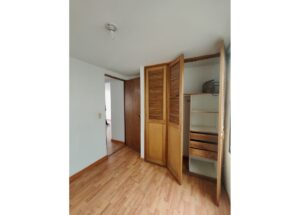 Bedroom corner with open wooden closet doors and built-in shelves; light wood floor and white walls