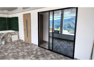 Interior space with tiled mosaic floor and large black-framed sliding glass doors opening to a balcony with mountain view in the distance