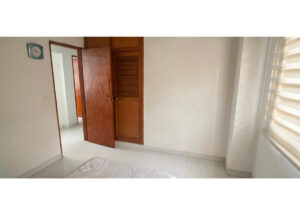Bedroom with white walls, a partially open wooden door near a built-in wardrobe, tiled floor, and a window with horizontal blinds on the right.