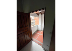 Doorway opens to a small balcony with red tile floor, white walls, and exposed wooden beams.