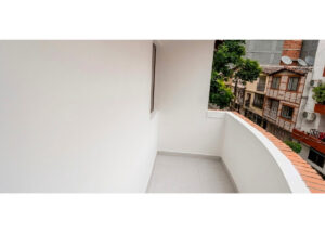 White corner balcony with curved railing and tiled floor, overlooking neighboring buildings and trees.