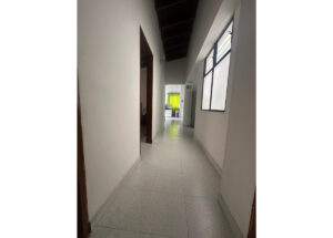 Long, bright hallway with white walls and tile floor; wooden ceiling beams run along the top toward a room with a green curtain at the far end