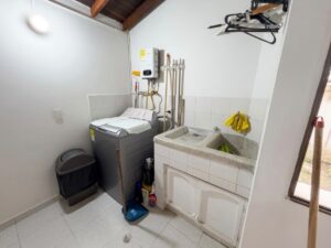 Compact laundry room with a top-loading washer beside a double-basin utility sink, cleaning supplies, and a mop leaning nearby.