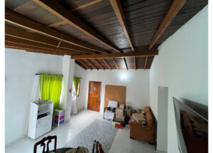 Living room with dark wood beam ceiling, white walls, green curtains, a brown sofa, and stacked boxes near the wall.