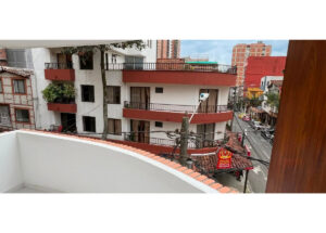 View from a balcony: white building with red curved balconies overlooking a street with shops and tangled power lines.