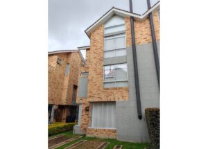 Brick townhouse with large windows and a 'For Sale' sign in the second-floor window overlooking a small lawn.