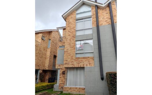 Brick townhouse with large windows and a 'For Sale' sign in the second-floor window overlooking a small lawn.