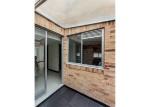 Brick-walled courtyard corner with a sliding glass door and a vented window, and dark tiled floor.